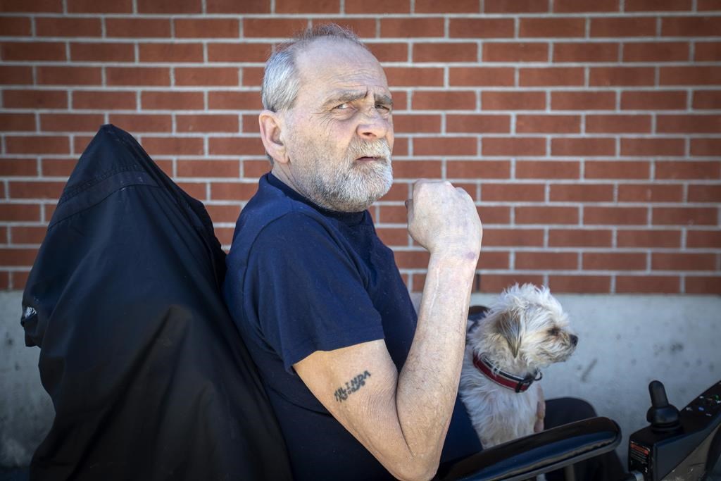 Will Towell holds his miniature terrier on his lap outside his temporary housing in Kingston, Ont., on Monday May 9, 2022.
