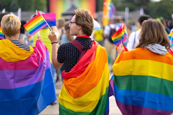 Wrapped in pride flags, a trio attends a Pride event in this stock image.