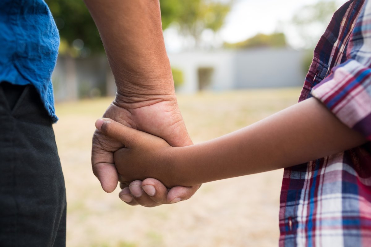 Cropped image of boy and grandfather holding hands while standing in yard