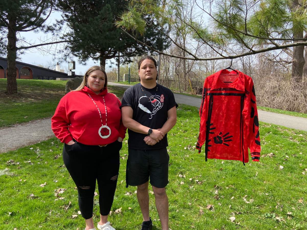 Elyssa Rose, Indigenous advocate and anti-human trafficking coordinator, and Dionovan Grosbeck, anti-human trafficking male lead, of Atlohsa Family Healing Services stand next to a red shirt dedicated to missing and murdered Indigenous men at the Red Dress Day in Ivey Park on May 5, 2022.
