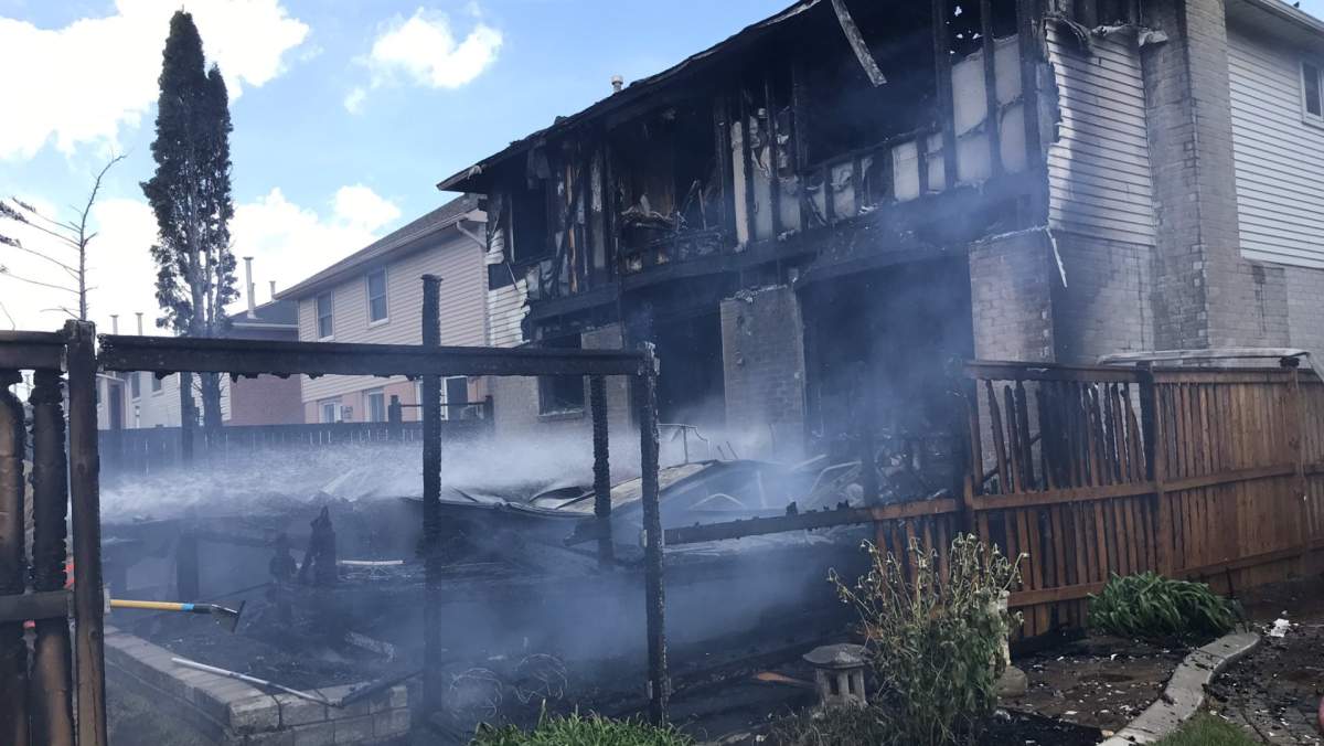 A two-storey house with the back totally charred and destroyed by fire, while firefighters aim a hose at the inside of the home to quell the blaze.