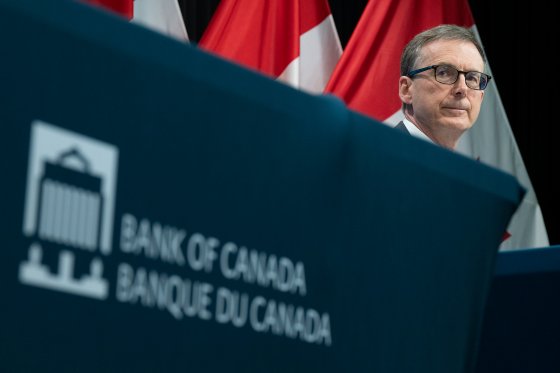 Bank of Canada Governor Tiff Macklem is pictured behind a sign with the bank's logo, and in front of a wall of Canadian flags.