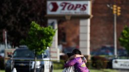 People hug in front of a sign marking the Buffalo supermarket where a mass shooting occurred.