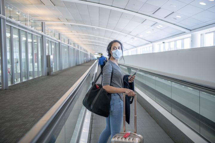 Young female wearing mask on a walking escalator at the airport.