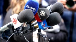 Microphones with media logos are visible on a stand at a press conference.