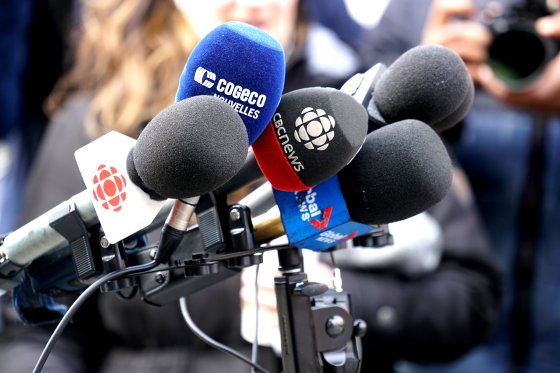 Microphones with media logos are visible on a stand at a press conference.