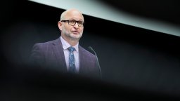 Justice Minister David Lametti stands at a press conference. He wears a grey suit against a black background.