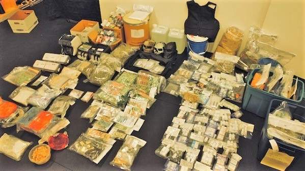 Packages of drugs and cash, money counters, body armour and skull-like face masks displayed across the floor.