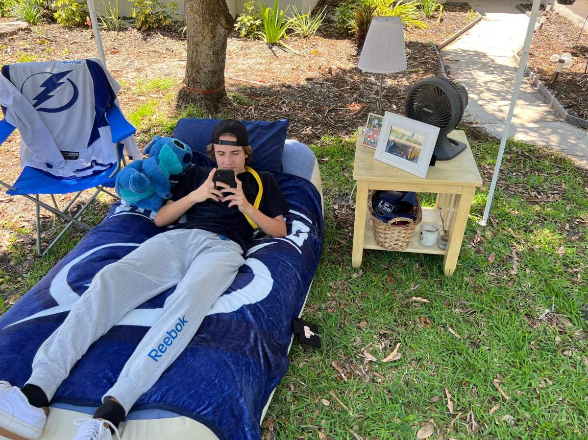 Logan Saul checks his phone on his bedroom that was moved into the front yard as part of a hockey-related prank.