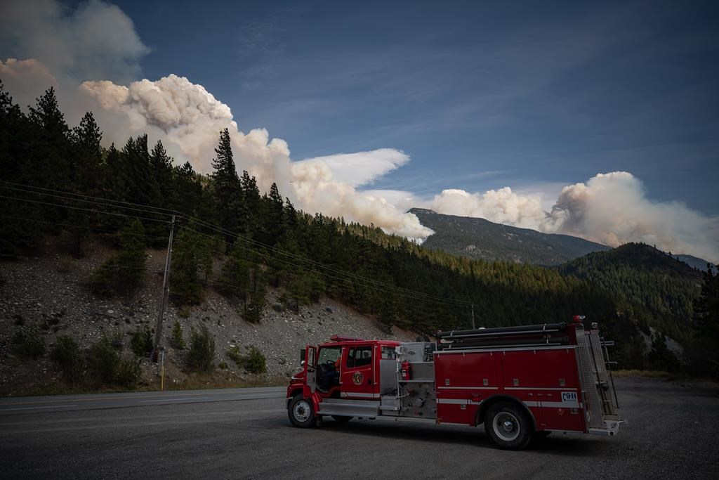 A man sits in a fire truck as the Lytton Creek wildfire burns in the mountains near Lytton, B.C., on Sunday, August 15, 2021. 