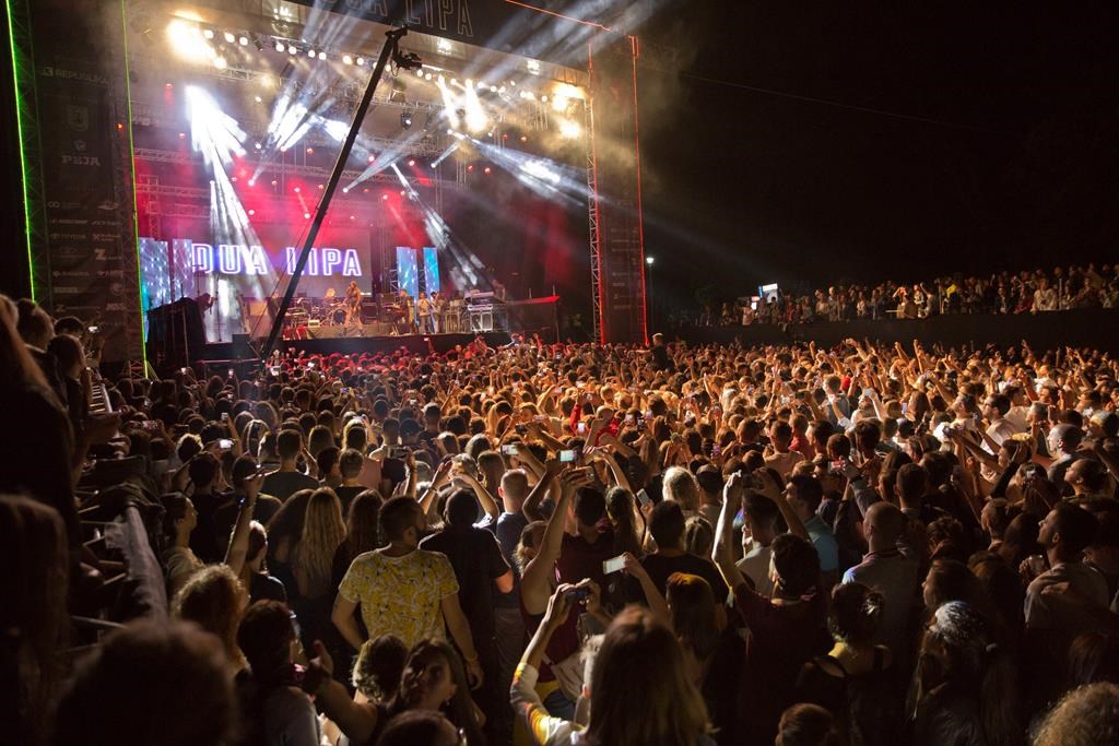 FILE - Fans cheer as British-Kosovar singer Dua Lipa performs on stage during her first concert held in Kosovo's capital Pristina, at the Germia Park on August 9, 2016. While Albania’s capital Tirana is bristling with preparations for holding an international music festival, its neighboring Kosovo’s counterpart Pristina is swarmed into political confrontations after losing it. The Sunny Hill Festival will be held this year Aug. 4-7 in Tirana instead of Pristina following a political controversy between Kosovo’s leftwing Self Determination Movement!-led government and opposition Democratic League of Kosovo running the capital. (AP Photo/Visar Kryeziu, File).
