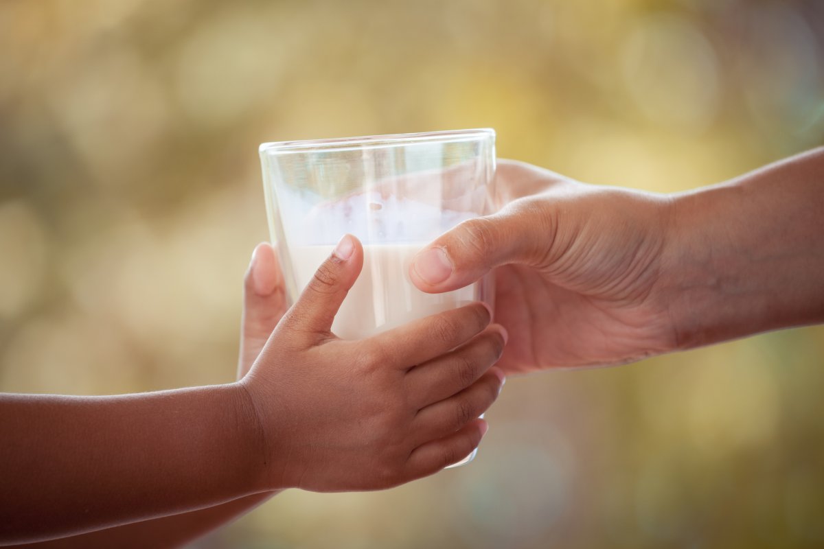 A stock photo shows an adult handing a child a glass of milk.