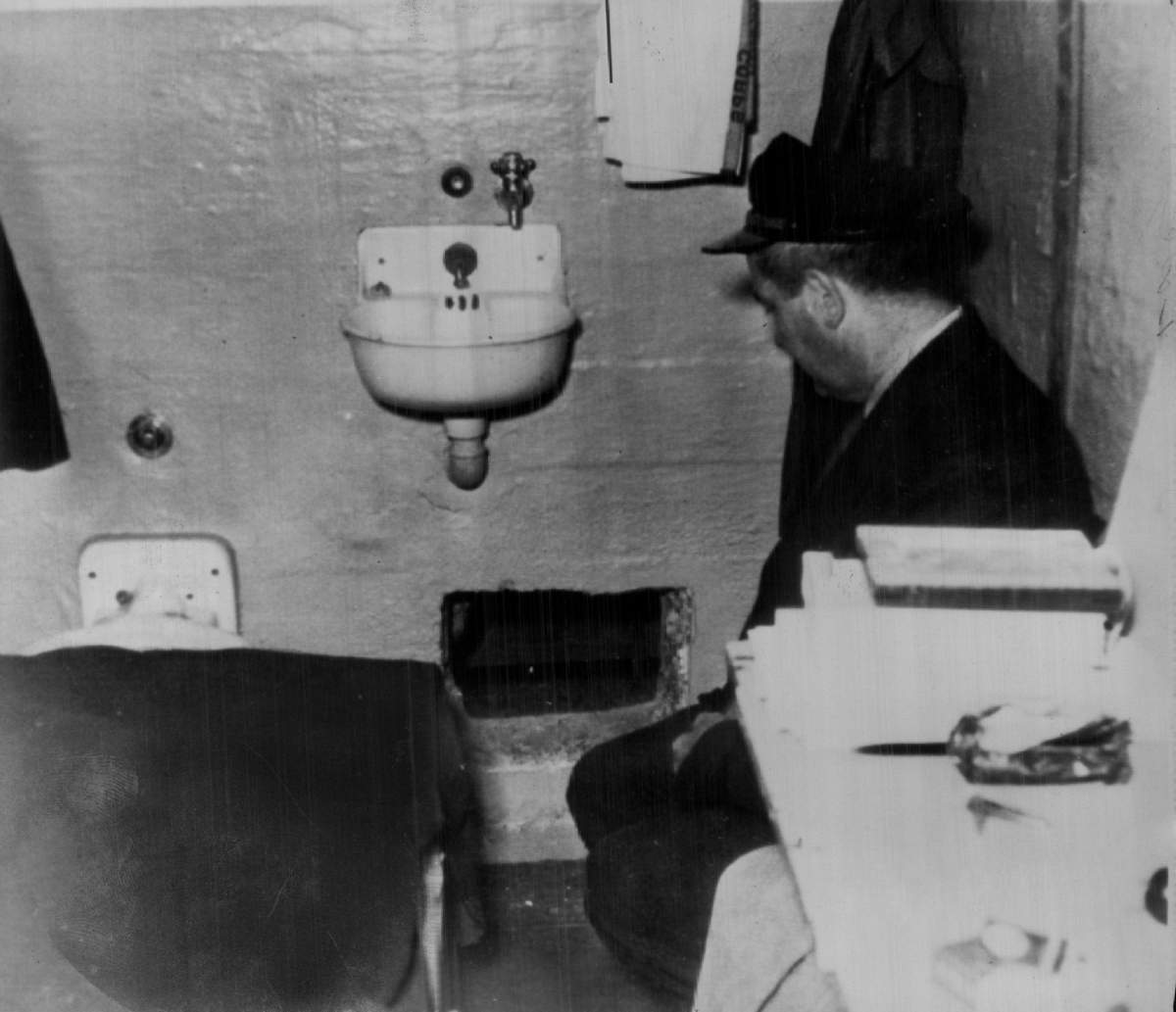 A prison guard kneels by hole in Frank Morris's cell through which he and John and Clarence Anglin escaped.