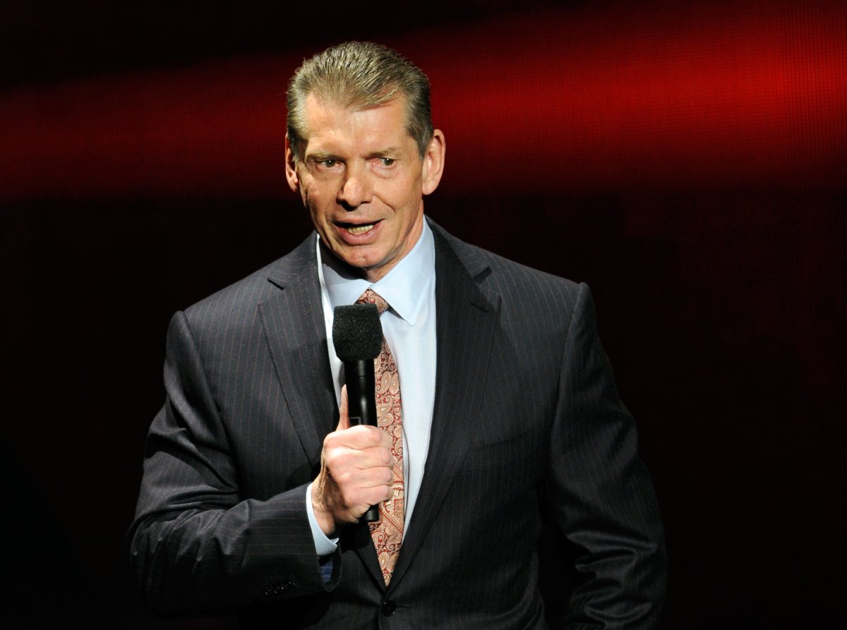 Vince McMahon holding a microphone and wearing a black suit.