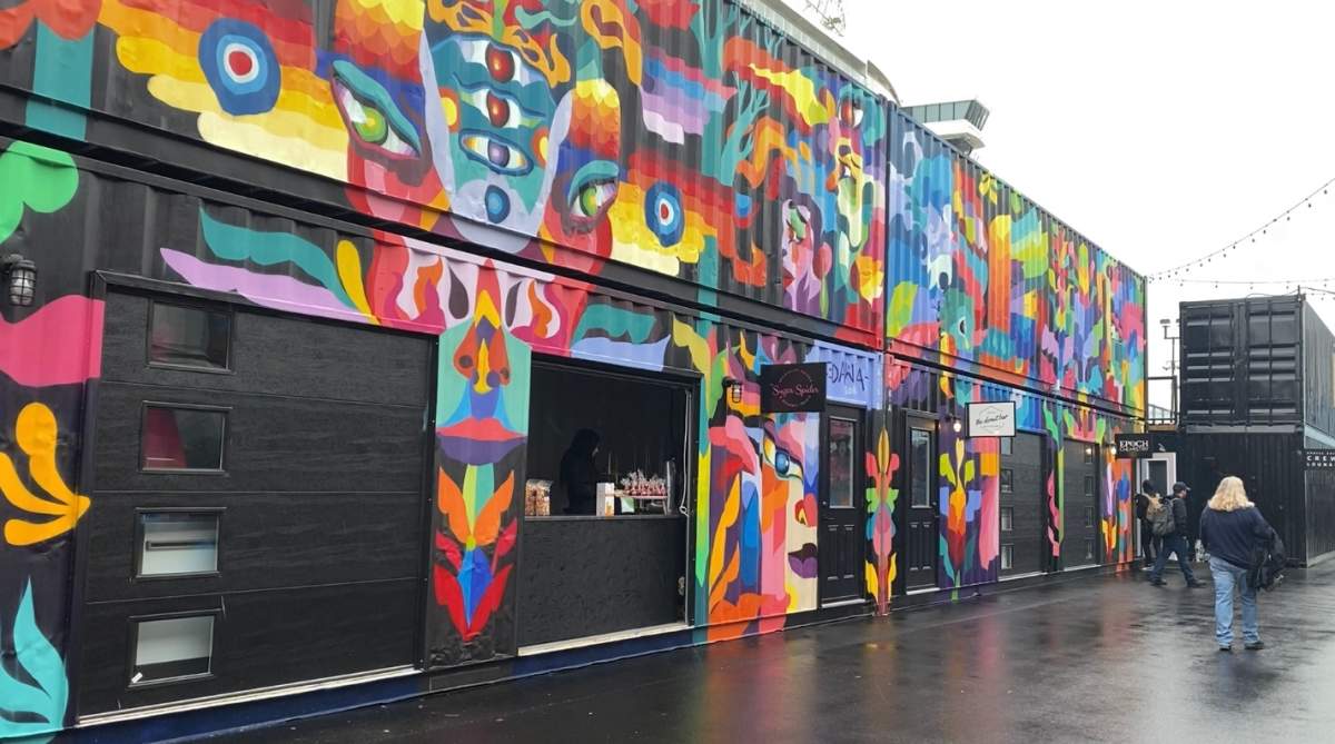 Work completed by several artists covers a row of shipping containers.