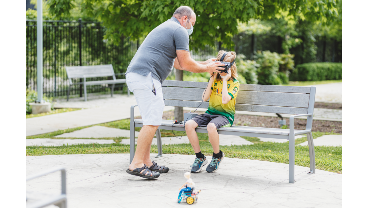 Mike Berube, a volunteer at the Ron Joyce Children’s Health Centre robotics club for outpatients, adjusts virtual reality goggles for a member used for maneuvering a remote control car.