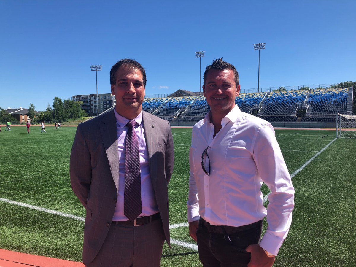 Mark Taylor and Roberto Di Donato smile in front of a soccer pitch