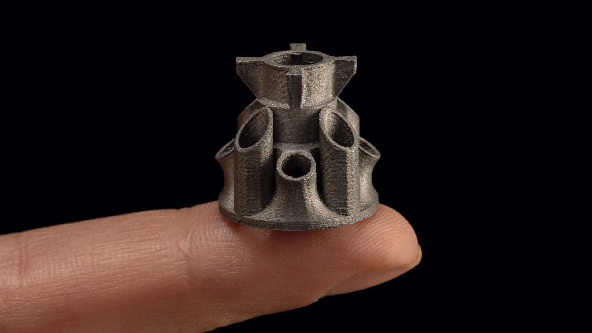 This photo shows an example of a tiny, but incredibly detailed 3D printed metal component made by Desktop Metal. In the photo, the individual print layers are clearly visible.