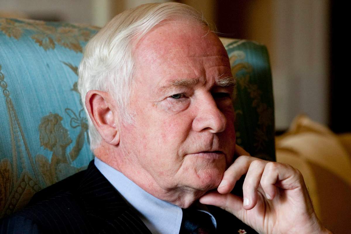 Former governor general David Johnson sits in a chair while wearing a suit.