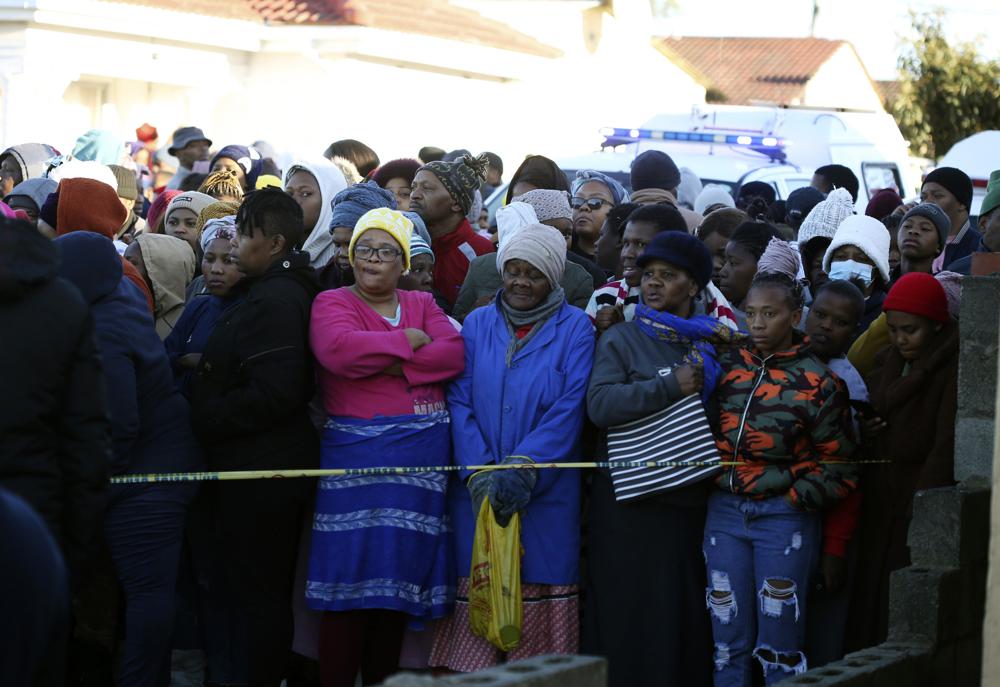 People stand behind a police cordon outside a nightclub in East London, South Africa, Sunday June 26, 2022. South African police are investigating the deaths of at least 20 people at a nightclub in the coastal town of East London early Sunday morning. It is unclear what led to the deaths of the young people, who were reportedly attending a party to celebrate the end of winter school exams.
