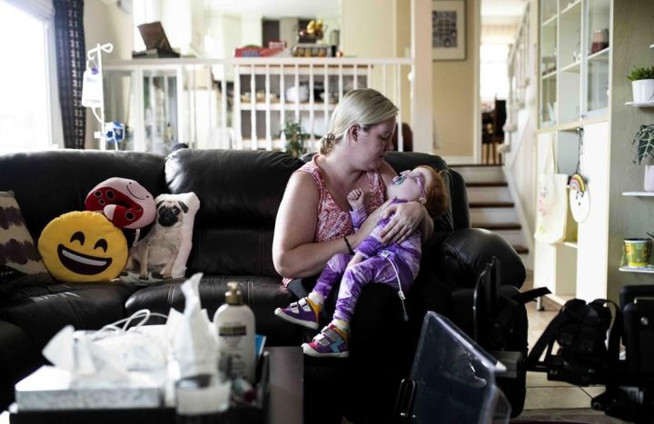 Amanda Jollymore rocks her daughter Mia, 2, who has an unknown genetic syndrome along with other diagnosed medical issues, as they sit on the couch at their home in Ottawa, on Monday, June 27, 2022. 
