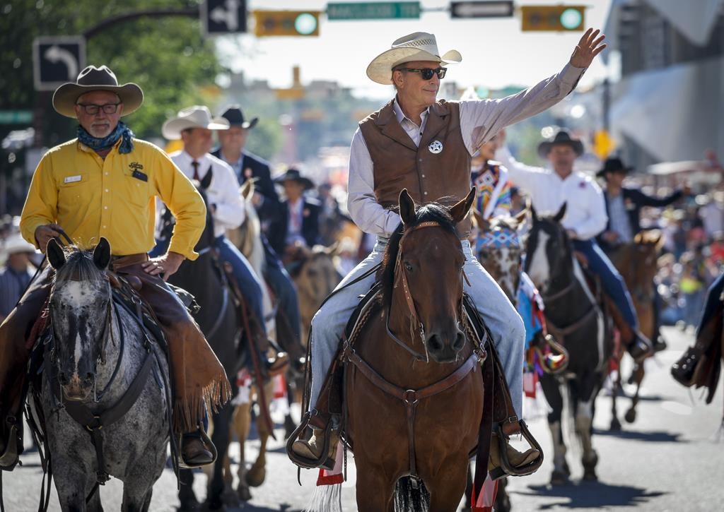 Parade marshal Kevin Costner, centre, waves to fans during the Calgary Stampede parade in Calgary, Friday, July 8, 2022.