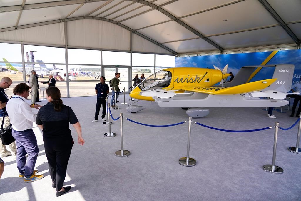 Visitors look at a model of the Wisk Aero autonomous aircraft, at the Farnborough Air Show fair in Farnborough, England, Tuesday, July 19, 2022. Some 1191 exhibitors from around the world show their newest developments in Future Flight, Space, Defence, Innovation, Sustainability and Workforce from July 18th until July 22, 2022.(AP Photo/Alberto Pezzali).