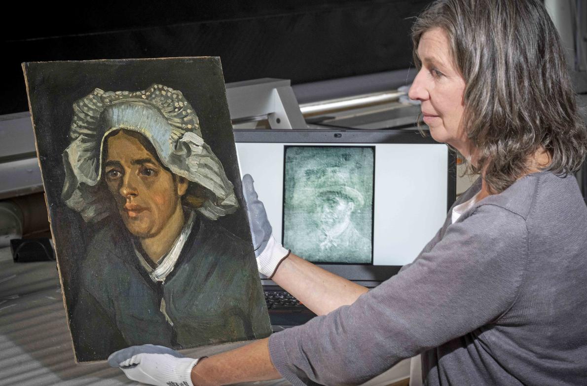 Senior Conservator Lesley Stevenson wears white gloves as she views "Head of a Peasant Woman" beside an X-ray image of the hidden Van Gogh self-portrait.