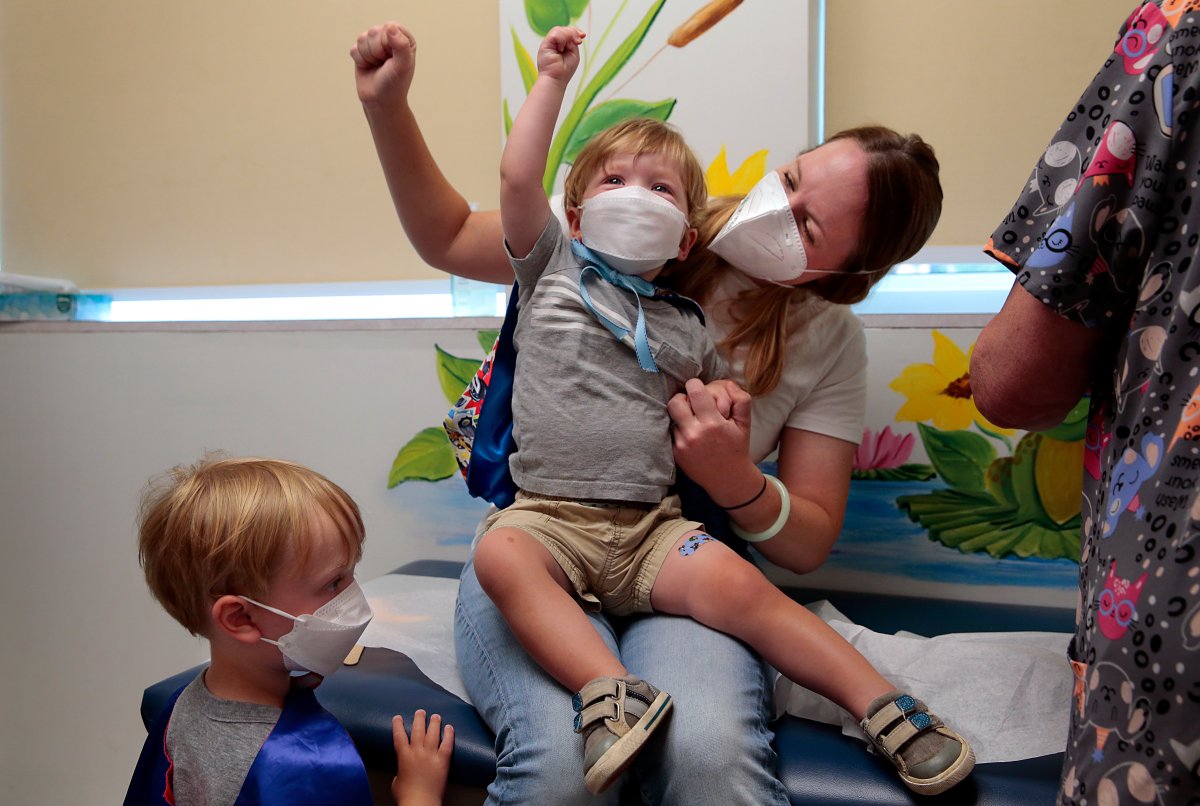 “Give it to the crowd!,” yells Jen Maddock as she raises her fist in celebration with son Will, 23 months, after the youngster received his COVID-19 vaccination at Southwest Pediatrics on Wednesday, June 22, 2022, in St. Louis. Will and his brother Jack, 3, waiting his turn at left, wore superhero capes for the occasion. Will was born with a heart defect during the pandemic and his family has remained isolated, with his mother quitting her job. “He hasn’t even met all of our family,” said Maddock.