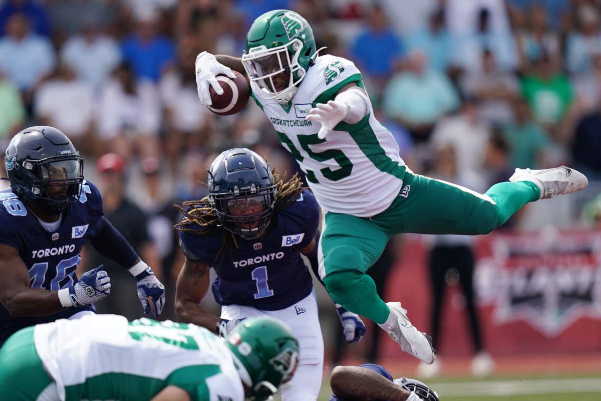 Saskatchewan Roughriders’ Jamal Morrow, right, leaps over a tackle in front of Toronto Argonauts Wynton McManis, left, and Shaq Richardson during the first half of CFL action at Acadia University in Wolfville, N.S., Saturday, July 16, 2022. THE CANADIAN PRESS/Darren Calabrese