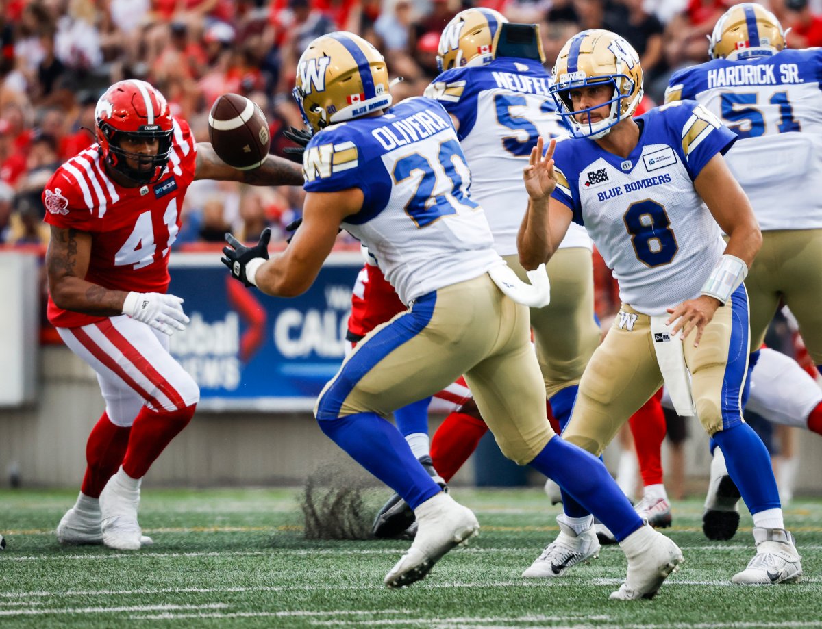 Winnipeg Blue Bombers quarterback Zach Collaros, right, tosses the ball to running back Brady Oliveira as Calgary Stampeders defensive lineman Mike Rose, left, looks on during first half CFL football action in Calgary, Saturday, July 30, 2022.