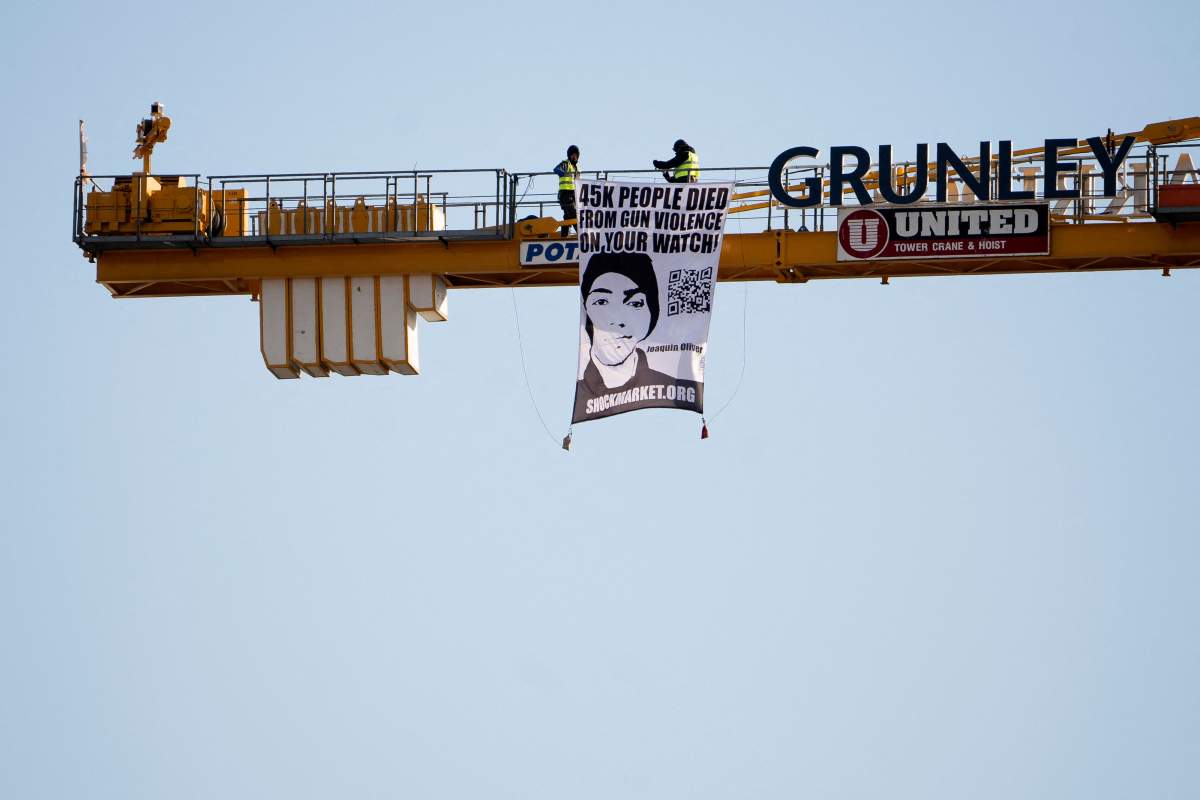 A wide shot of a crane and large poster. Manuel Oliver displays a banner calling on government officials to prioritize gun violence prevention from a construction crane near the White House in Washington, DC, on February 14, 2022.