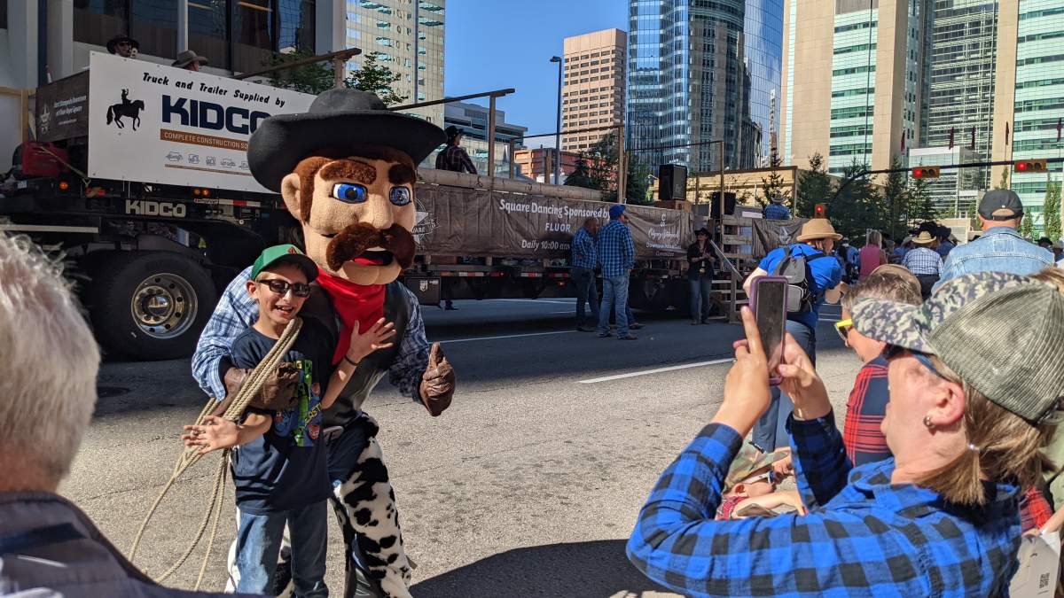 Onlookers pose for a photo with one of the mascots during the Calgary Stampede Parade on July 8, 2022.