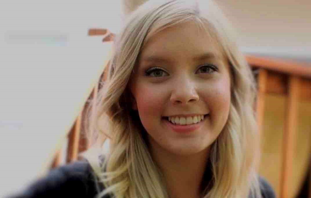 Caitlin Jensen smiles at the camera. She has long blonde hair and is wearing a dark top.