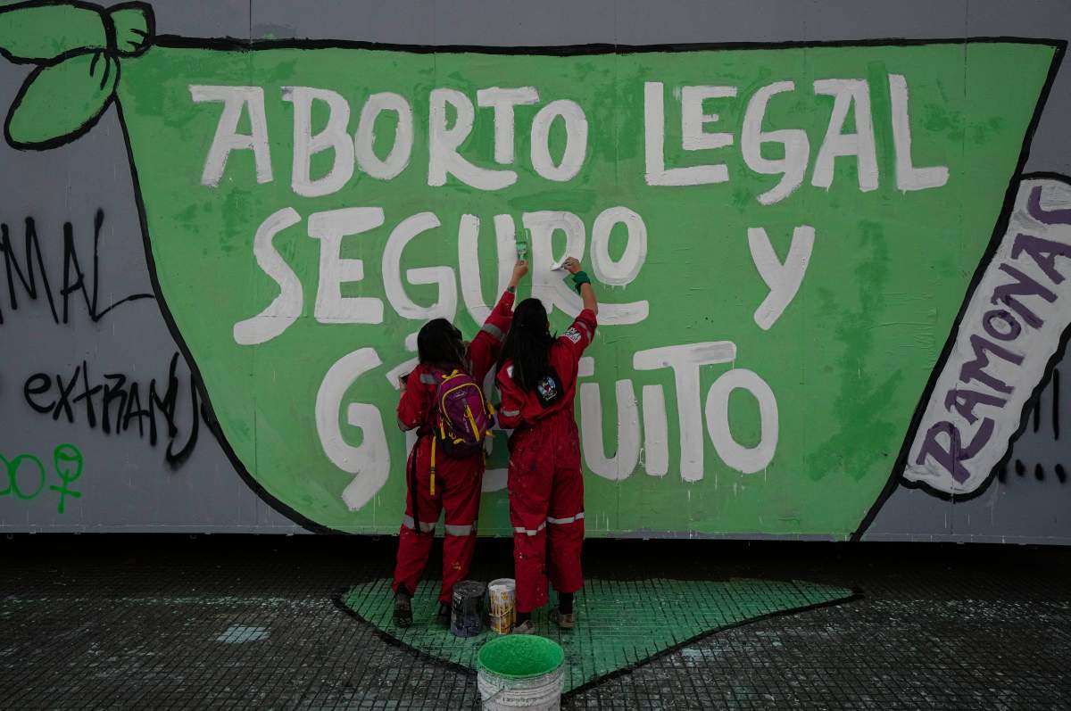 Abortion rights protestors paint a sign on a wall in green in Chile.