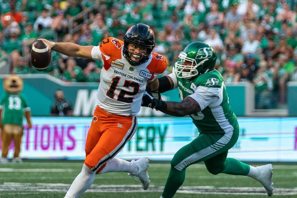 BC Lions quarterback Nathan Rourke (12) evades a tackle from Saskatchewan Roughriders defensive lineman Charleston Hughes (39) during the second quarter of CFL football action in Regina, on Friday, July 29, 2022. Rourke has been named a CFL top performer of the week for the third time this season.THE CANADIAN PRESS/Heywood Yu.