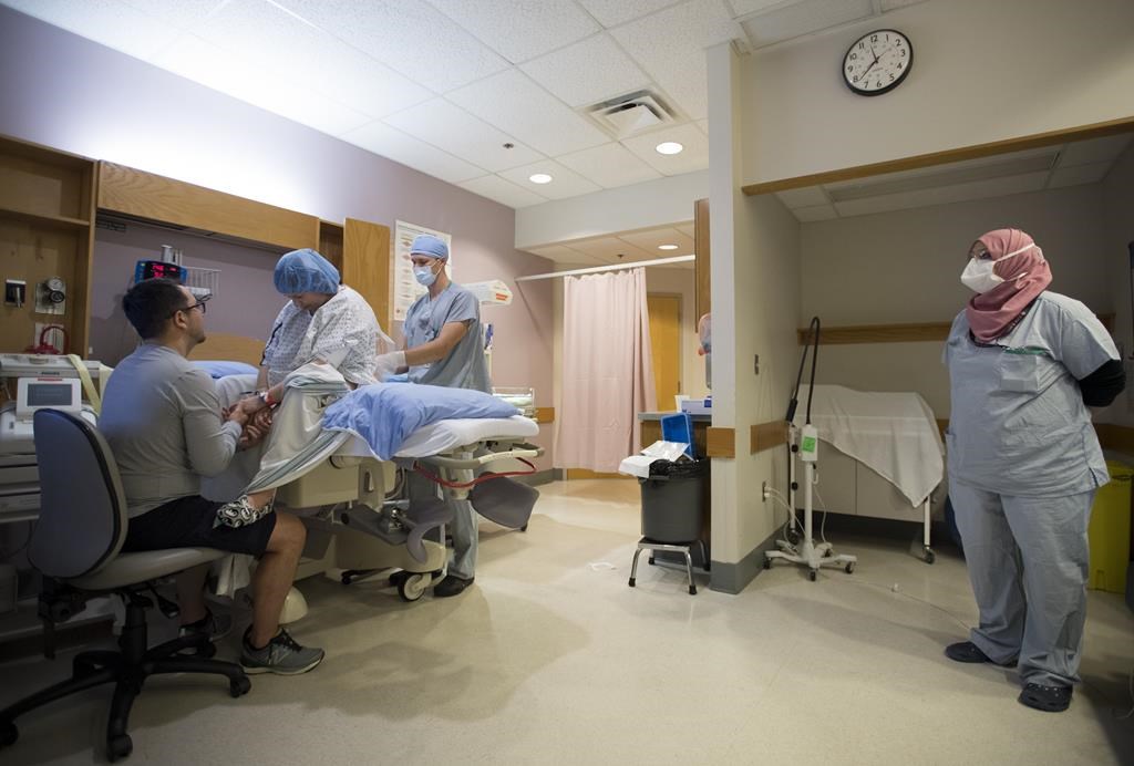 A nurse wearing a protective face mask looks on as Kate Chong receives an epidural from the on call anesthesiologist at St. Paul's hospital in downtown Vancouver, Saturday, June 13, 2020. 