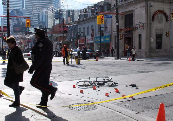 A police officer escorts a woman from the scene of a garbage truck-bicycle collision that left a woman, 38, fighting for her life in downtown Toronto on Tuesday Nov. 13, 2012.  