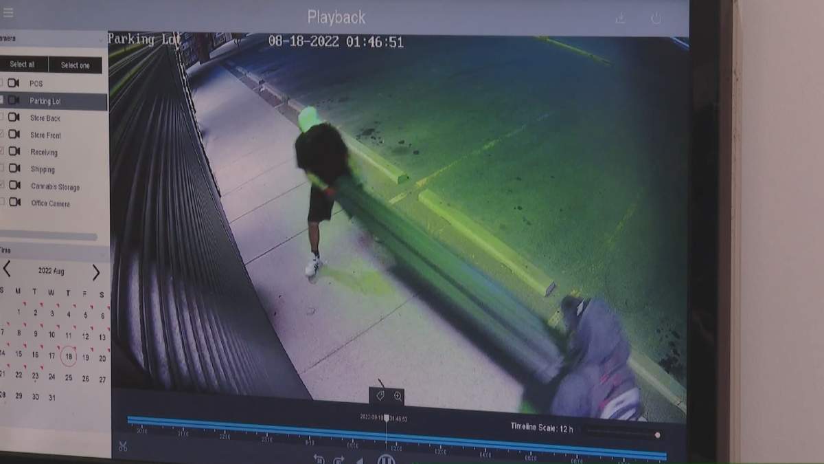 Two people are seen disassembling security shutters on Omkara Cannabis in Calgary on Aug. 18, 2022, in an apparent attempt to gain entry.