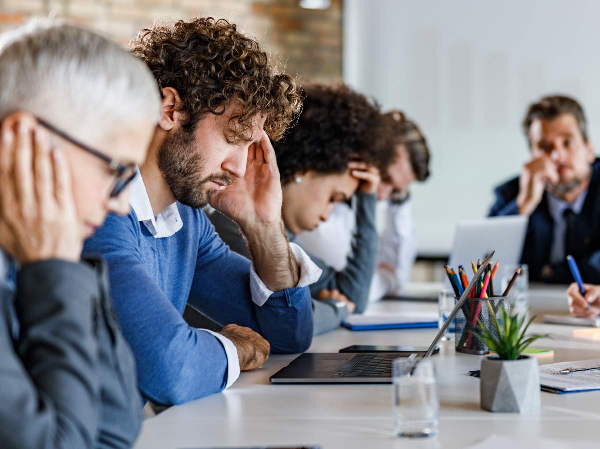 Group of entrepreneurs feeling frustrated during a meeting in the office. Focus is on man with headache.