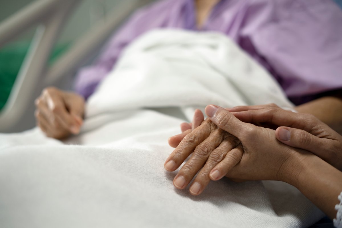 Image of daughter holding her mother's hand in a hospital bed.