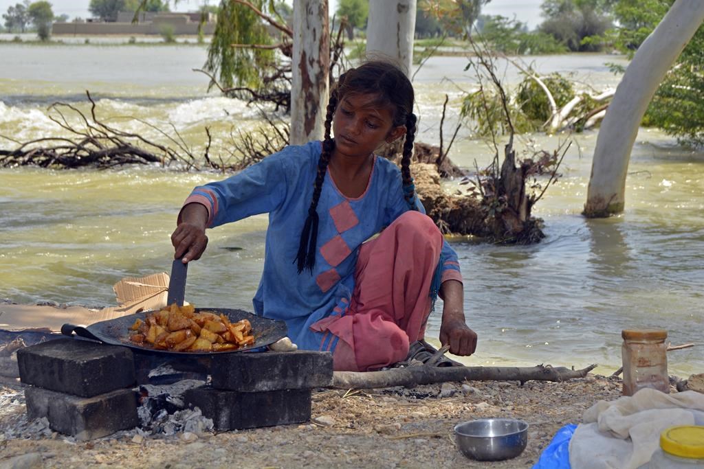 A displaced girl cooks potatoes next to floodwaters after taking refuge from her family's flood-hit home, in Multan, Pakistan, Wednesday, Aug. 31, 2022. Officials in Pakistan raised concerns Wednesday over the spread of waterborne diseases among thousands of flood victims as flood waters from powerful monsoon rains began to recede in many parts of the country. 