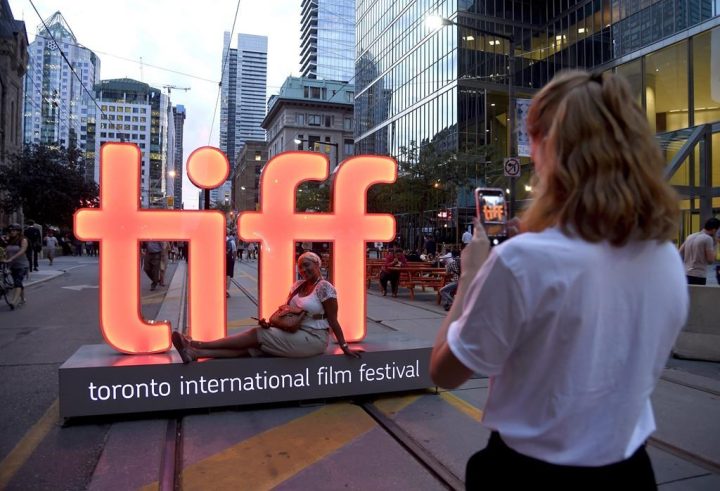 A volunteer takes a photo in front of a festival sign on day 1 of the Toronto International Film Festival on Thursday, Sept. 6, 2018, in Toronto. The Toronto International Film Festival returns to its full form after three years with in-person red carpets and a full slate of screenings, but many questions are swirling about the future of the film industry. 