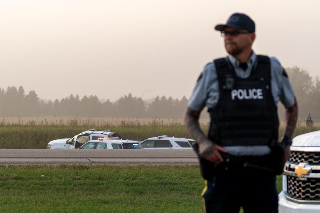 Police and investigators are seen at the side of the road outside Rosthern, Sask., on Wednesday, Sept. 7, 2022. Myles Sanderson, a suspect in a deadly series of stabbings in Saskatchewan, was caught by police on a highway, arrested, and died, RCMP said Wednesday. THE CANADIAN PRESS/Heywood Yu.