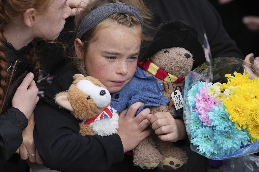 A young girl holds a Paddington bear and a Corgi dog stuffed toys while waiting to watch the Procession of Queen Elizabeth's coffin from the Palace of Holyroodhouse to St Giles Cathedral on the Royal Mile in Edinburgh, Scotland, Monday, Sept. 12, 2022.