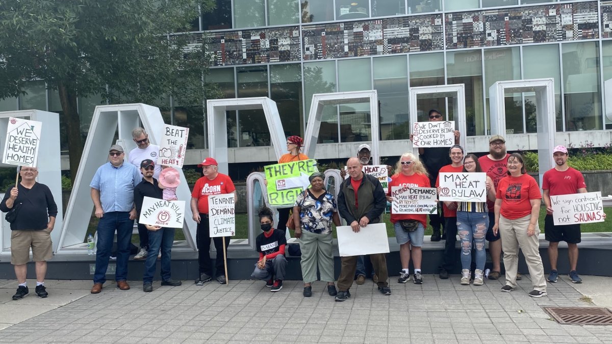 Members of Hamilton ACORN stand in front of the Hamilton sign in front of city hall, holding signs related to addressing extreme heat in apartment buildings.