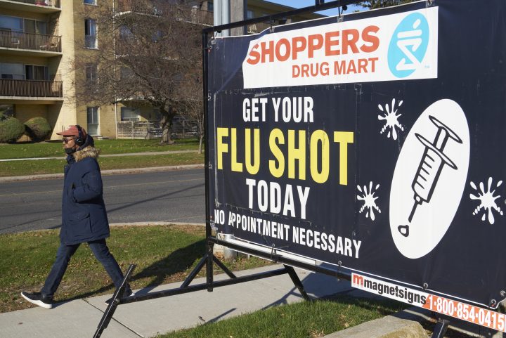 A man walks past a Shoppers Drug Mart sign promoting the flu shot in Toronto on Nov. 14, 2020.