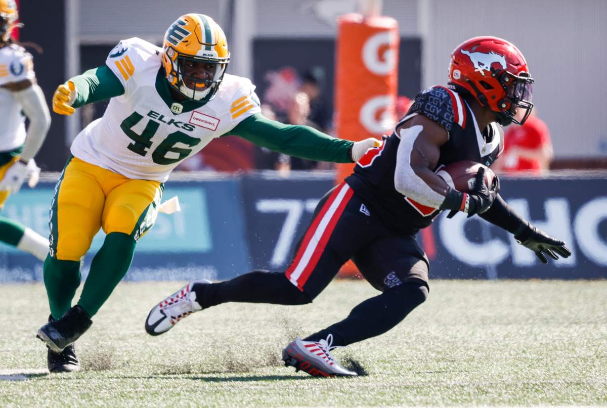 Edmonton Elks linebacker Nate Evans, left, grabs for Calgary Stampeders running back Ka’Deem Carey during first half CFL football action in Calgary, Alta., Monday, Sept. 5, 2022.