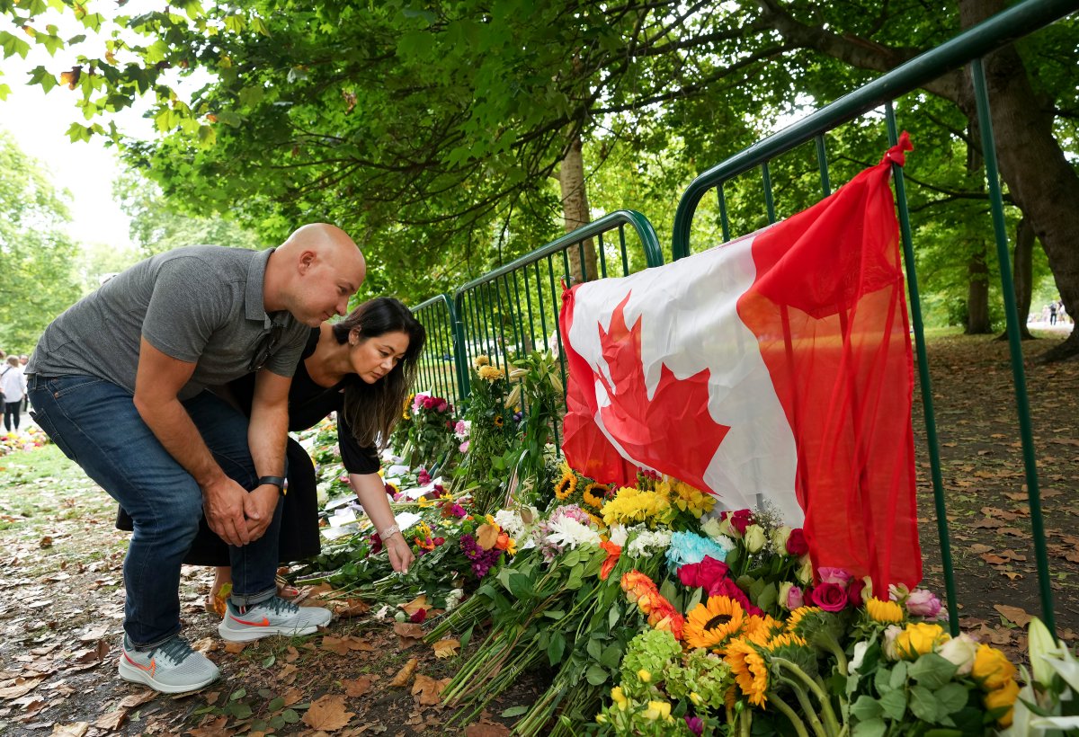 Canadians Kersten Samolczyk, right, and her husband Carlie Samolczyk who now reside in the United Kingdom place flowers by a Canadian flag as thousands of mourners lay flowers as people pay their respects near the gates of Buckingham Palace in London on Sunday, September 11, 2022.