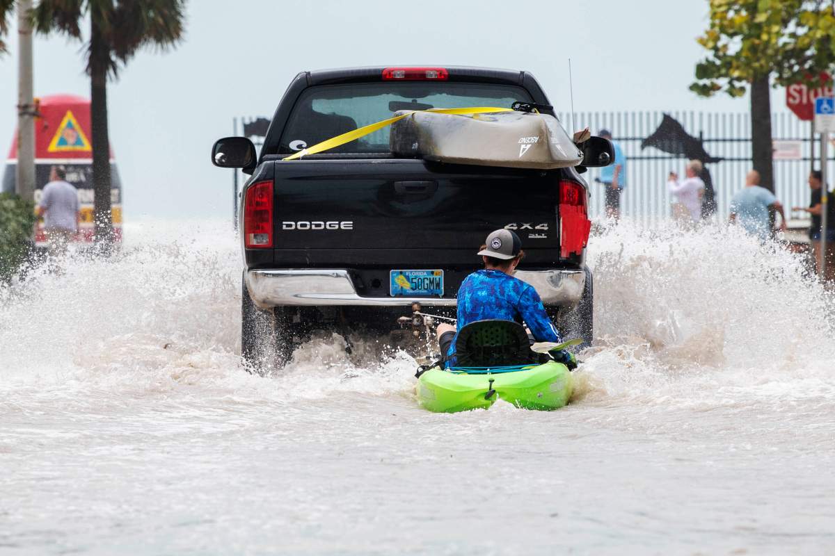 A truck pulls a man on a kayak on a low-lying road after flooding in aftermath of Hurricane Ian, in Key West, Fla. on a street near the Southernmost Point buoy, Wednesday afternoon, Sept. 28, 2022. (AP Photo/Mary Martin)